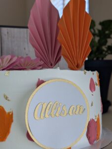 Topper de nombre con abanicos de papel sobre un pastel blanco